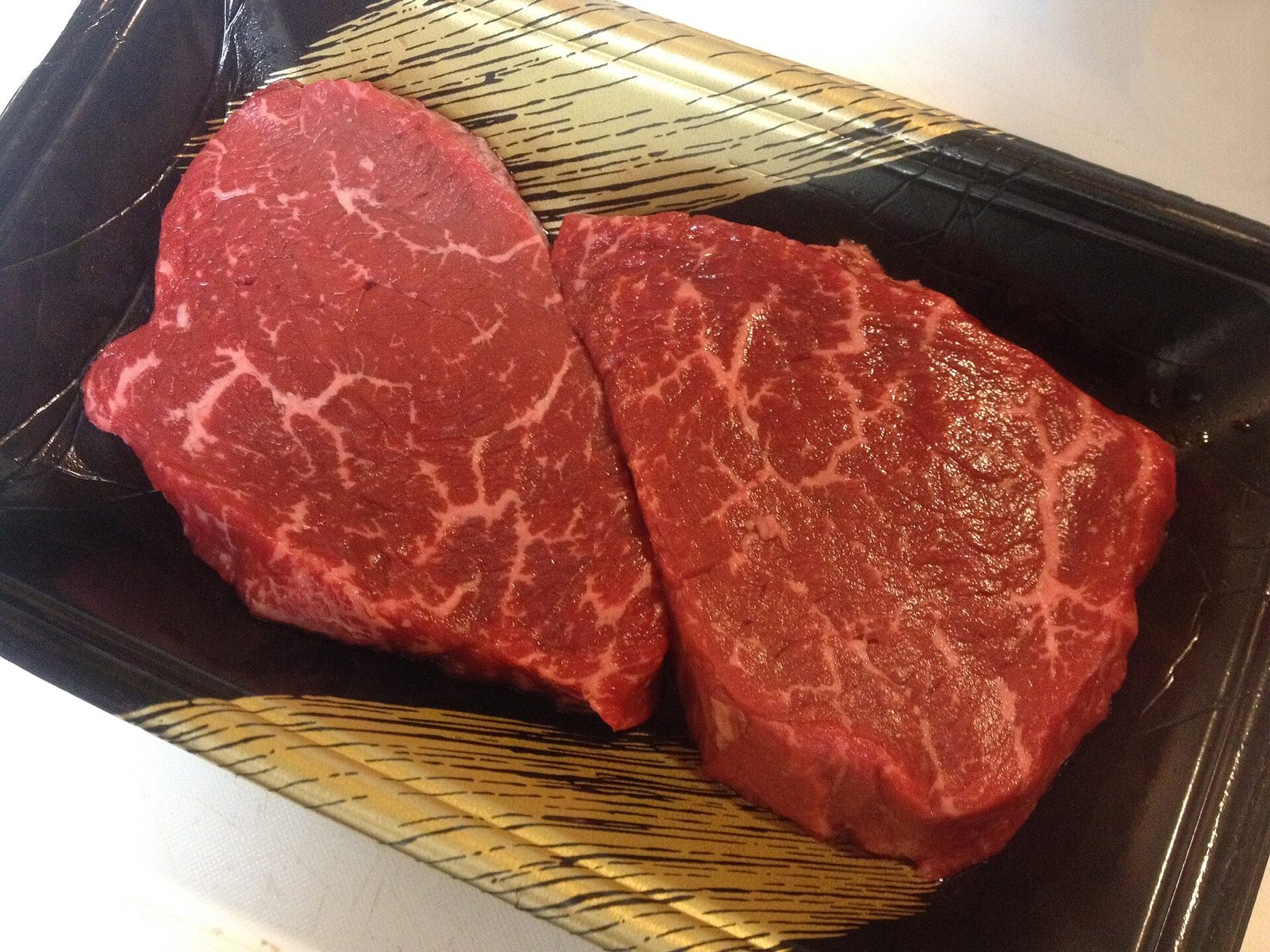 Two raw wagyu steaks with fine white marbling in a black tray