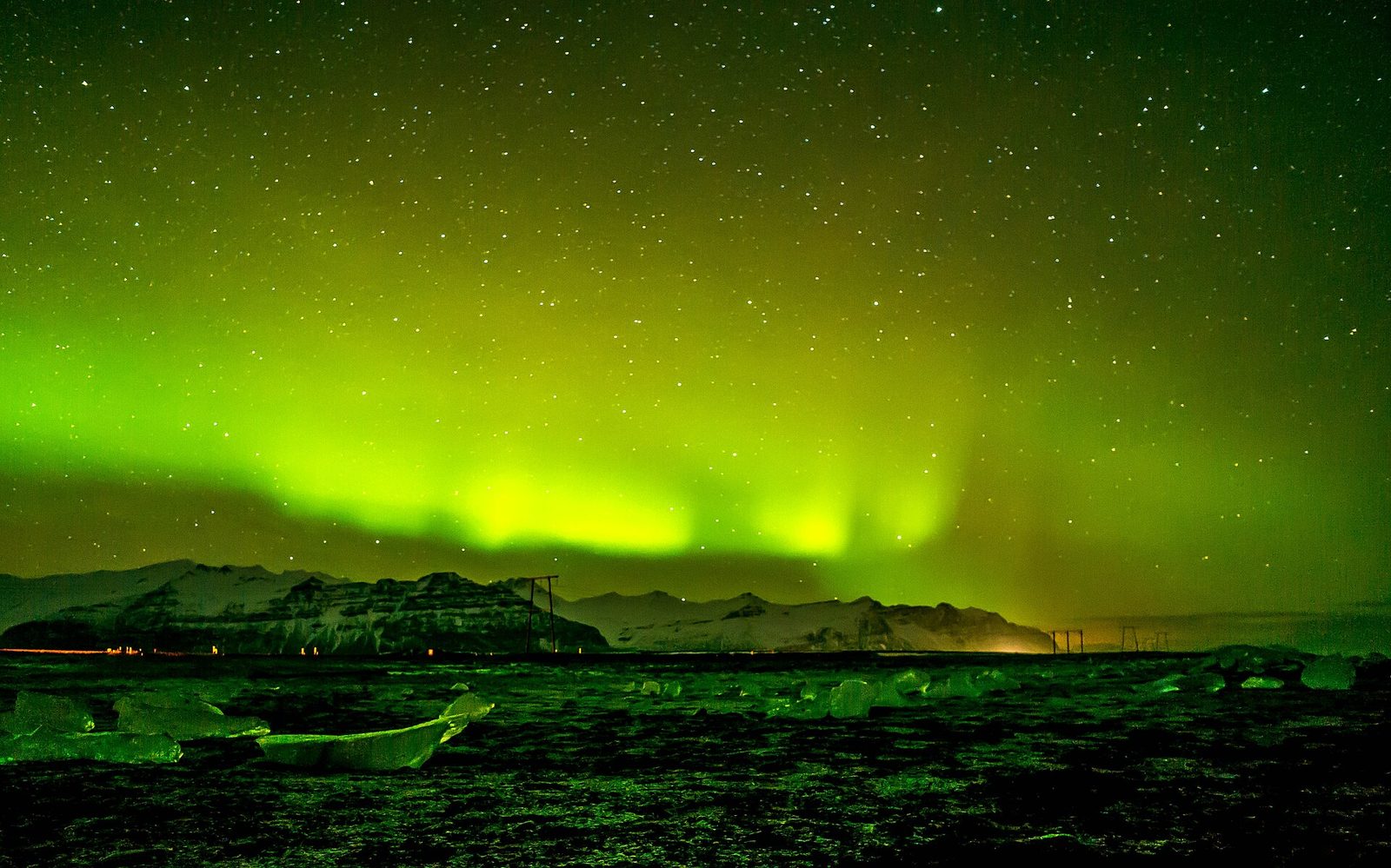 Green aurora over snowy mountains and ice chunks on a black beach