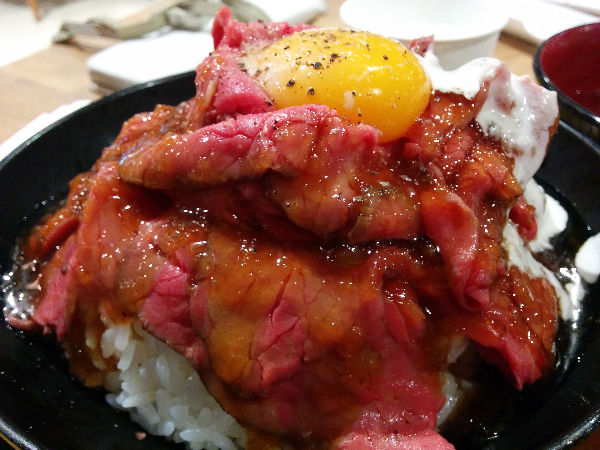 Rare sliced roast beef piled on rice with a raw egg yolk and sauce