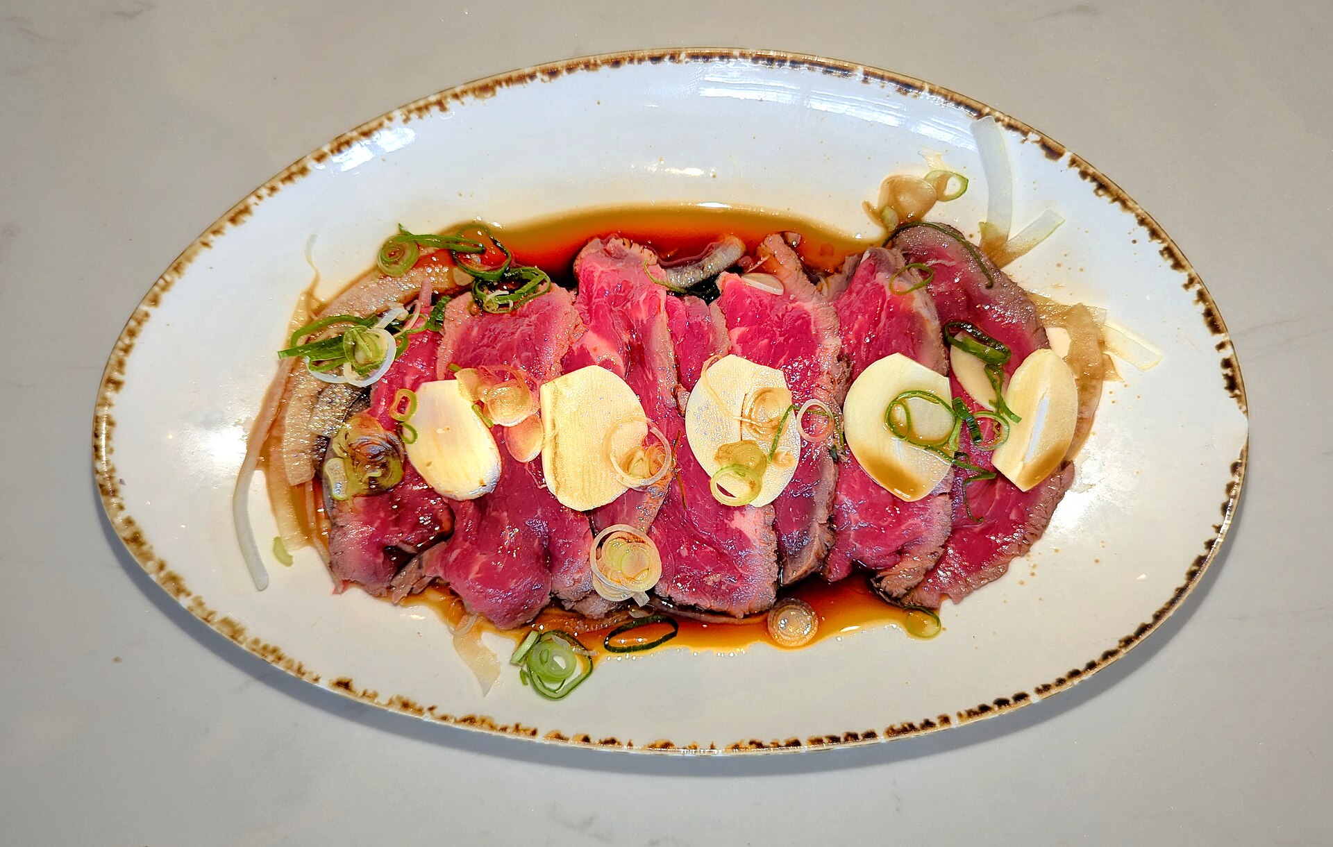 Sliced beef tataki with a seared edge and rare centre in a ponzu-style sauce