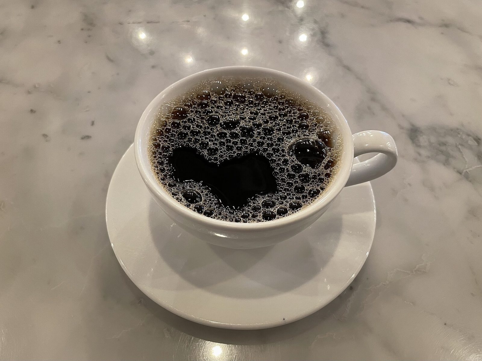 Black coffee in a white cup on a marble café table